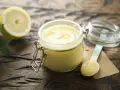 Un tarro de dulce de limón casero, con una cuchara de madera y un limón cortado al fondo, sobre una mesa de madera rústica.