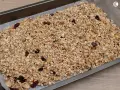 Granola de avena casera lista para hornear, con frutos secos y pasas, extendida en una bandeja.