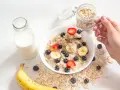 Un tazón de avena con fresas, arándanos y plátano. Un frasco de avena y una botella de leche sugieren cómo se hacen los copos de avena.