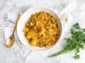Un tazón de arroz con acelgas, patatas y alubias blancas, servido con una cuchara dorada y perejil fresco.