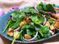 Ensalada de espinacas frescas con crutones, cebolla morada y aderezo en un plato azul.