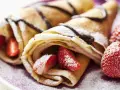 Deliciosos crepes sin huevo rellenos de fresas y bañados en chocolate, espolvoreados con azúcar glas.