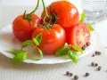 Tomates frescos con gotas de agua, albahaca y granos de pimienta, ingredientes naturales para productos antiinflamatorios.