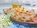Deliciosa berenjena rellena gratinada, adornada con piñones y brotes frescos, lista para ser disfrutada.
