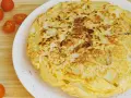 Tortilla vegana dorada y esponjosa, con trozos de patata visibles, servida en plato blanco. Tomates cherry al lado.