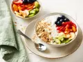 Un tazón de yogur cremoso con granola crujiente, arándanos, fresas, plátano, kiwi y melocotón.
