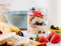 Deliciosa avena nocturna en un frasco con fresas, arándanos y almendras. Plátanos y galletas de arroz al lado.
