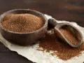 Un cuenco de madera lleno de teff cereal y una pala de madera con más granos.
