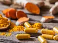 Cápsulas amarillas y polvo de cúrcuma sobre madera rústica, destacando los beneficios de la curcuma en capsulas.