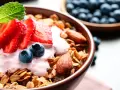 Un tazón de qué es la granola, cubierto con yogur de fresa, fresas, arándanos y almendras.