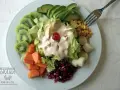Ensalada tropical con aguacate, kiwi, papaya, palmitos, maíz y granada, cubierta de aderezo cremoso y una cereza.