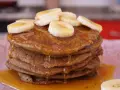 Pila de tortitas de avena y plátano, cubiertas con rodajas de plátano y sirope dorado. ¡Un desayuno delicioso!