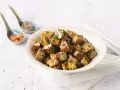 Tazón lleno de cubos dorados de tofu marinado, espolvoreados con cebollín y semillas.