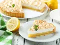 Un delicioso pastel de limón con merengue dorado, acompañado de limones frescos y una servilleta a cuadros verdes. Los ingredientes del lemon pie lucen perfectos.