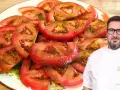Un chef sonriente presenta un plato de tomate aliñado, fresco y jugoso, con un aderezo verde y aceite.
