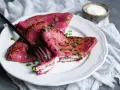 Crepes rosados ​​rellenos de queso crema, perfectos para recetas con remolacha cruda. Decorados con cebollín y acompañados de una porción de crema agria.