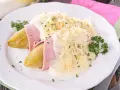Endivias al horno envueltas en jamón, cubiertas con una cremosa salsa bechamel y queso rallado, adornadas con perejil fresco.
