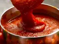 Salsa de tomate italiano espesa cayendo de una cuchara a un cuenco metálico, rodeado de tomates frescos.