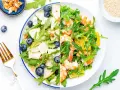 Dos ensaladas de rucula: una con pera, arándanos y nueces; la otra con gambas y naranja.