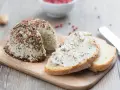 Queso vegano receta: un bloque de queso cremoso cubierto de pimienta y hierbas, servido con rebanadas de pan.