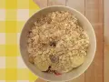 Un tazón de porridge de avena con plátano, fresas y pasas, servido sobre un mantel a cuadros amarillos y blancos.