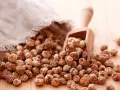Un saco de tela deja caer una gran cantidad de chufas sobre una mesa de madera. Una cuchara de madera recoge algunas de estas pequeñas y arrugadas semillas.