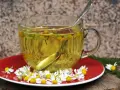 Té de manzanilla en una taza de cristal, con flores frescas y una cuchara. Es bueno para el estómago.