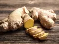 Raíces de jengibre enteras y en rodajas sobre madera. Descubre qué es el jengibre y sus usos.