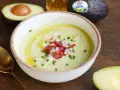Un cremoso gazpacho de aguacate, adornado con tomate picado, cebolla y cebollino, con un chorrito de aceite de oliva.