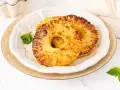 Dos rodajas de piña a la plancha, doradas y caramelizadas, servidas en un plato blanco con hojas de menta.