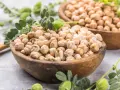 Dos cuencos de madera llenos de garbanzos secos, con hojas verdes y vainas. Los garbanzos tienen fibra, ¡un alimento saludable!
