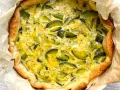 Quiche de calabacín recién horneada, con masa dorada y relleno cremoso salpicado de trozos verdes.