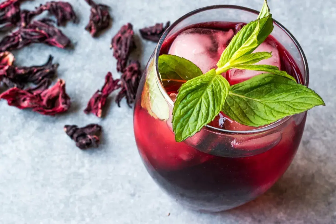 Refrescante vaso de agua de jamaica con hielo y menta, rodeado de flores secas de hibisco.