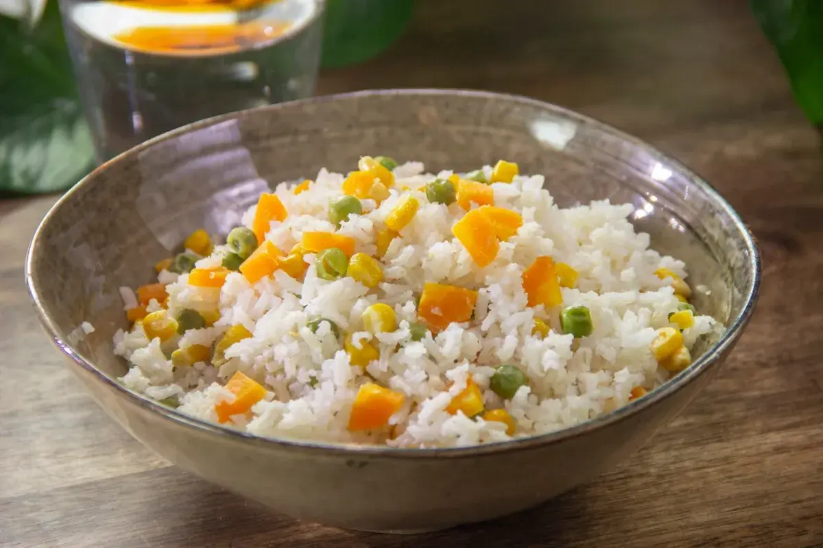 Un tazón de arroz blanco con trozos de zanahoria, guisantes y maíz. Un plato sencillo y colorido de arroz con verduras.