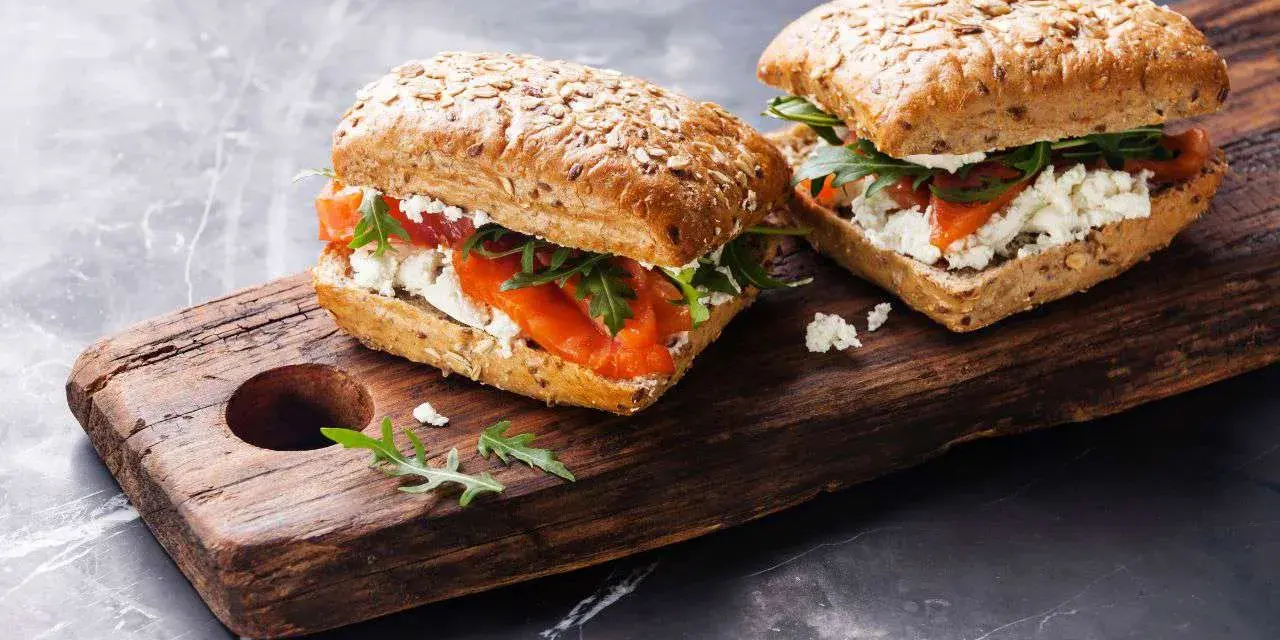 Dos sándwiches de salmón y queso fresco en pan integral, perfectos para un menú de ayuno intermitente.