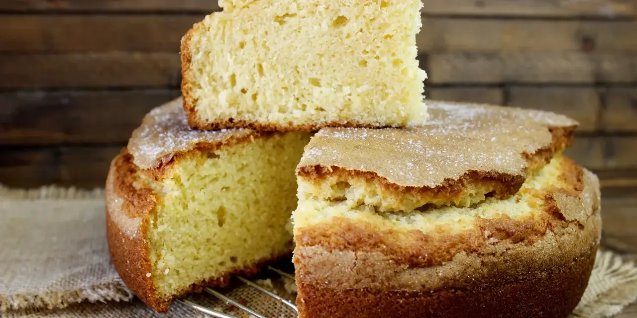 El bizcocho de limón de la abuela, esponjoso y dorado, con una capa de azúcar espolvoreada. Un trozo descansa sobre el pastel principal.