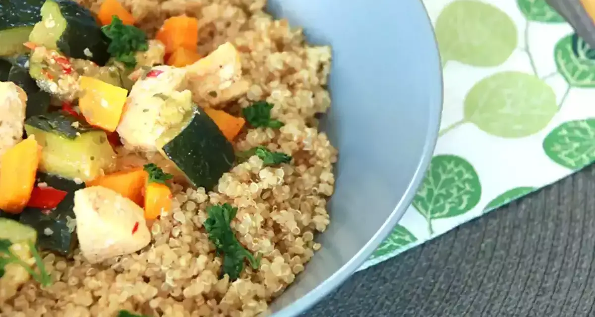 Un tazón de quinoa con pollo y verduras salteadas, como calabacín y zanahoria.
