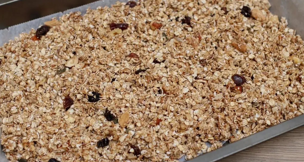 Granola de avena casera lista para hornear, con frutos secos y pasas, extendida en una bandeja.