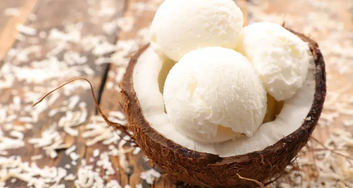 Delicioso helado con leche de coco servido en una cáscara de coco, espolvoreado con coco rallado sobre una mesa de madera.
