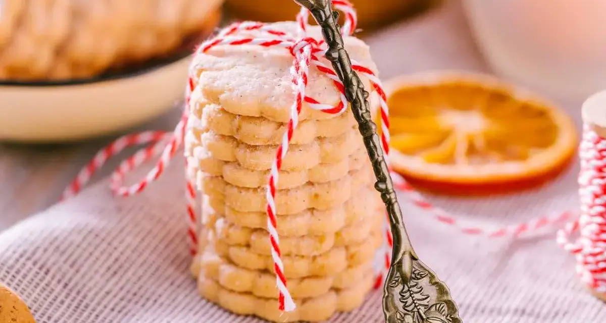 Deliciosas galletas de naranja, apiladas y atadas con hilo rojo y blanco. Una rodaja de naranja y una cuchara antigua completan la escena.