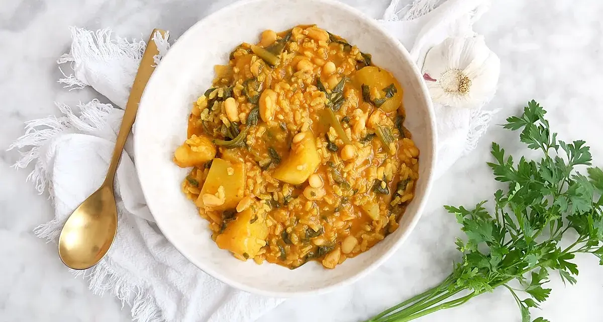 Un tazón de arroz con acelgas, patatas y alubias blancas, servido con una cuchara dorada y perejil fresco.