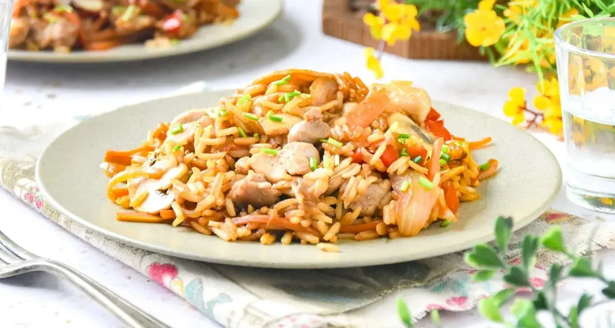 Un delicioso wok de verduras y arroz con trozos de pollo y champiñones, adornado con cebollino fresco.