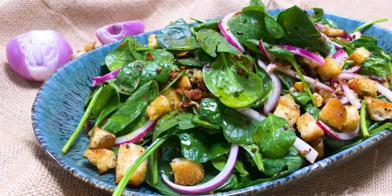 Ensalada de espinacas frescas con crutones, cebolla morada y aderezo en un plato azul.