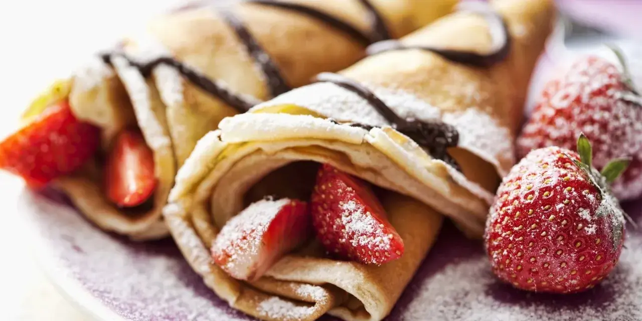 Deliciosos crepes sin huevo rellenos de fresas y bañados en chocolate, espolvoreados con azúcar glas.