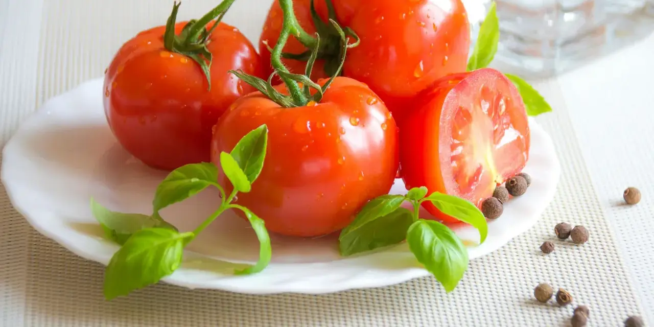 Tomates frescos con gotas de agua, albahaca y granos de pimienta, ingredientes naturales para productos antiinflamatorios.