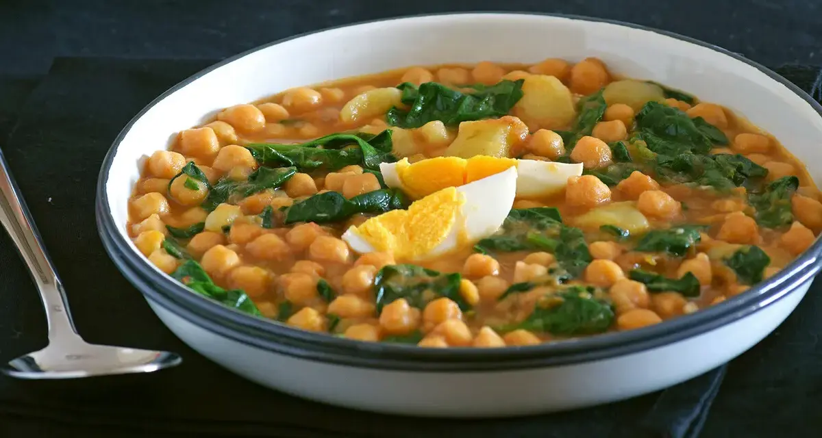 Plato humeante de garbanzos con espinacas y huevo duro, una deliciosa receta de garbanzos tradicional.