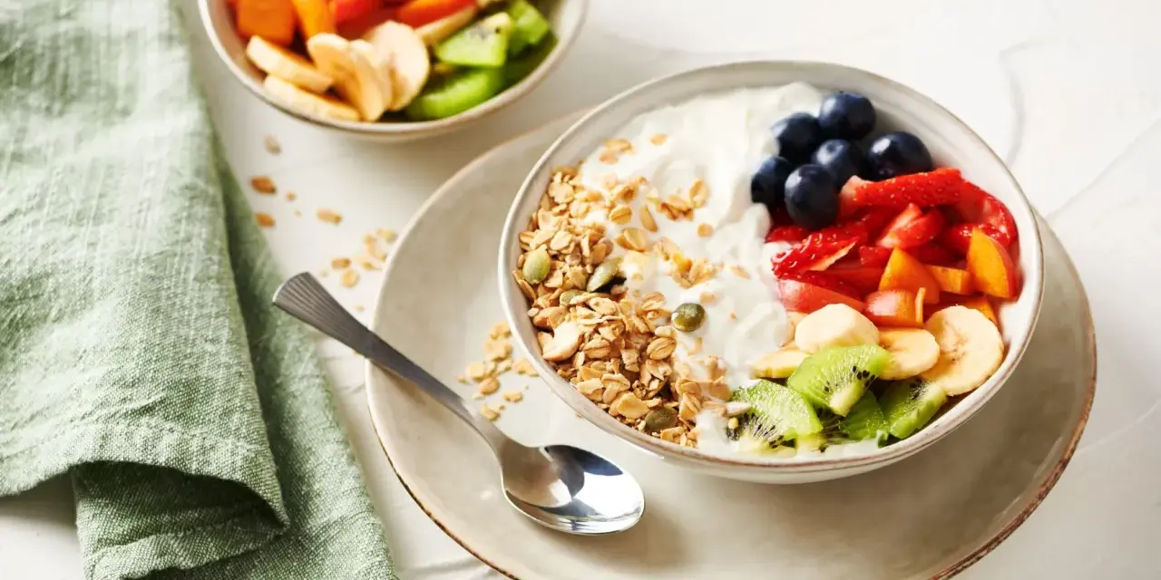 Un tazón de yogur cremoso con granola crujiente, arándanos, fresas, plátano, kiwi y melocotón.