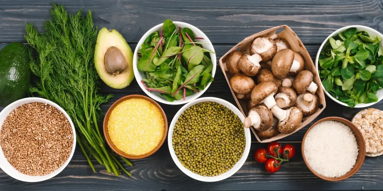 Variedad de alimentos ricos en proteinas vegetales: aguacate, hinojo, lentejas, champiñones, arroz, tomates y hojas verdes.
