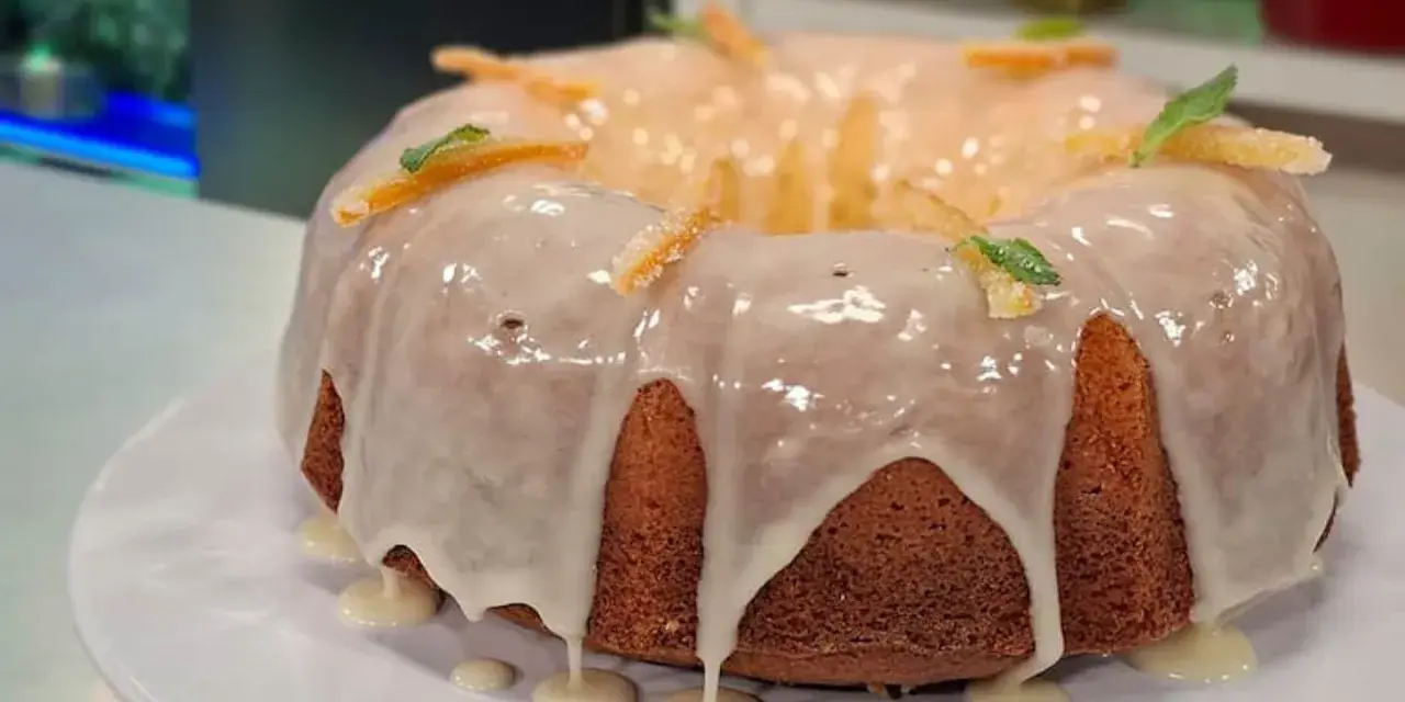 Delicioso budín de naranja con glaseado blanco y decorado con cáscaras de naranja confitada y hojas de menta.