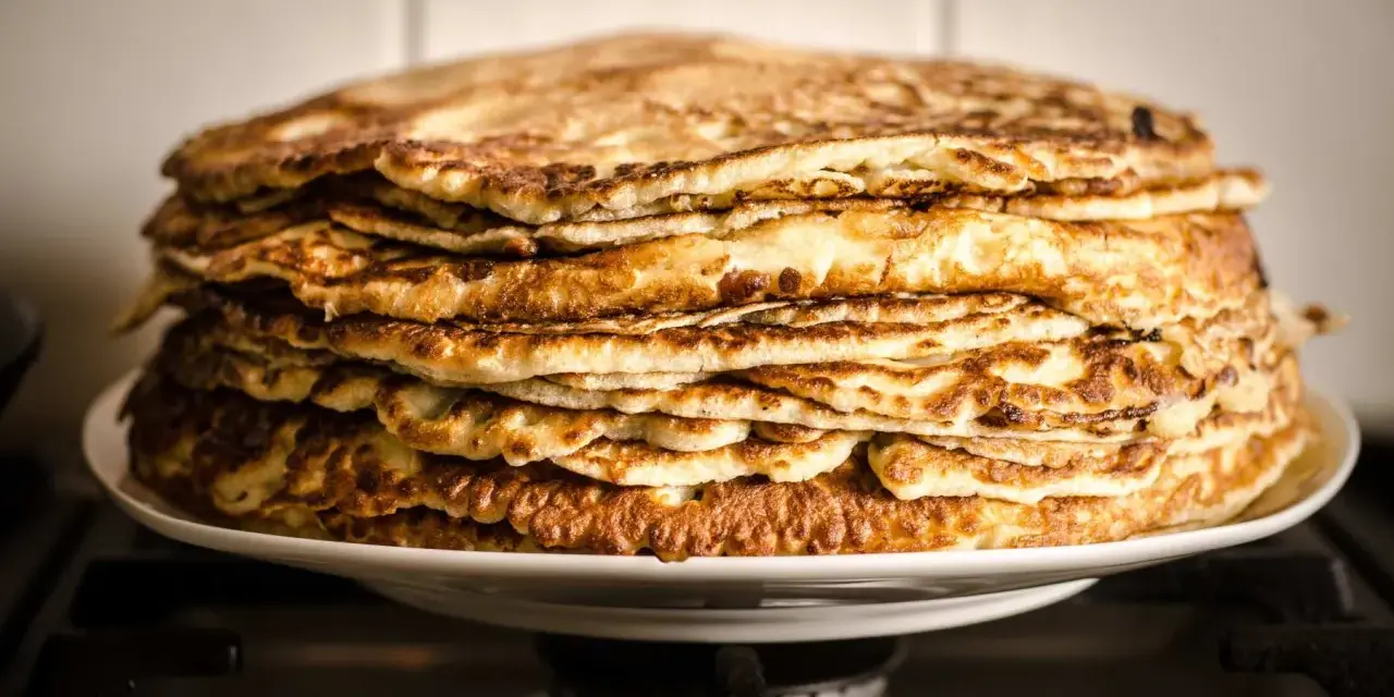 Montón de deliciosos pancakes sin gluten, dorados y esponjosos, apilados en un plato blanco.